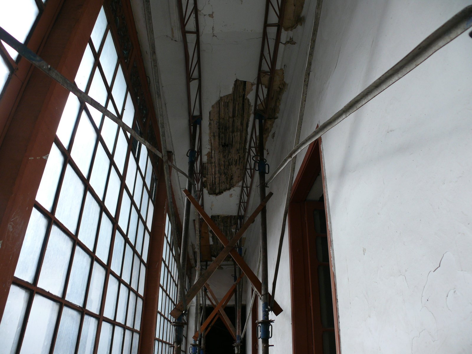 Corredor acristalado con deterioro visible en el cielo raso antes de la restauración